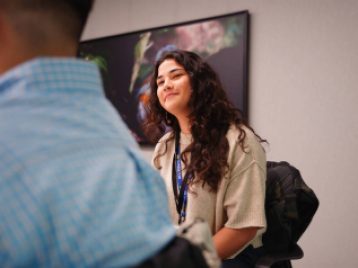 UM student sitting in a meeting room, smiling at another student who's off camera